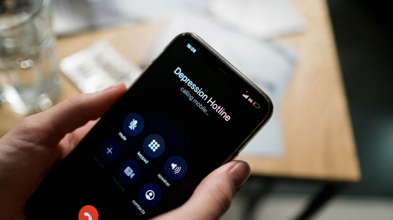Hands holding a smartphone. The screen shows an outgoing call to a "depression hotline".