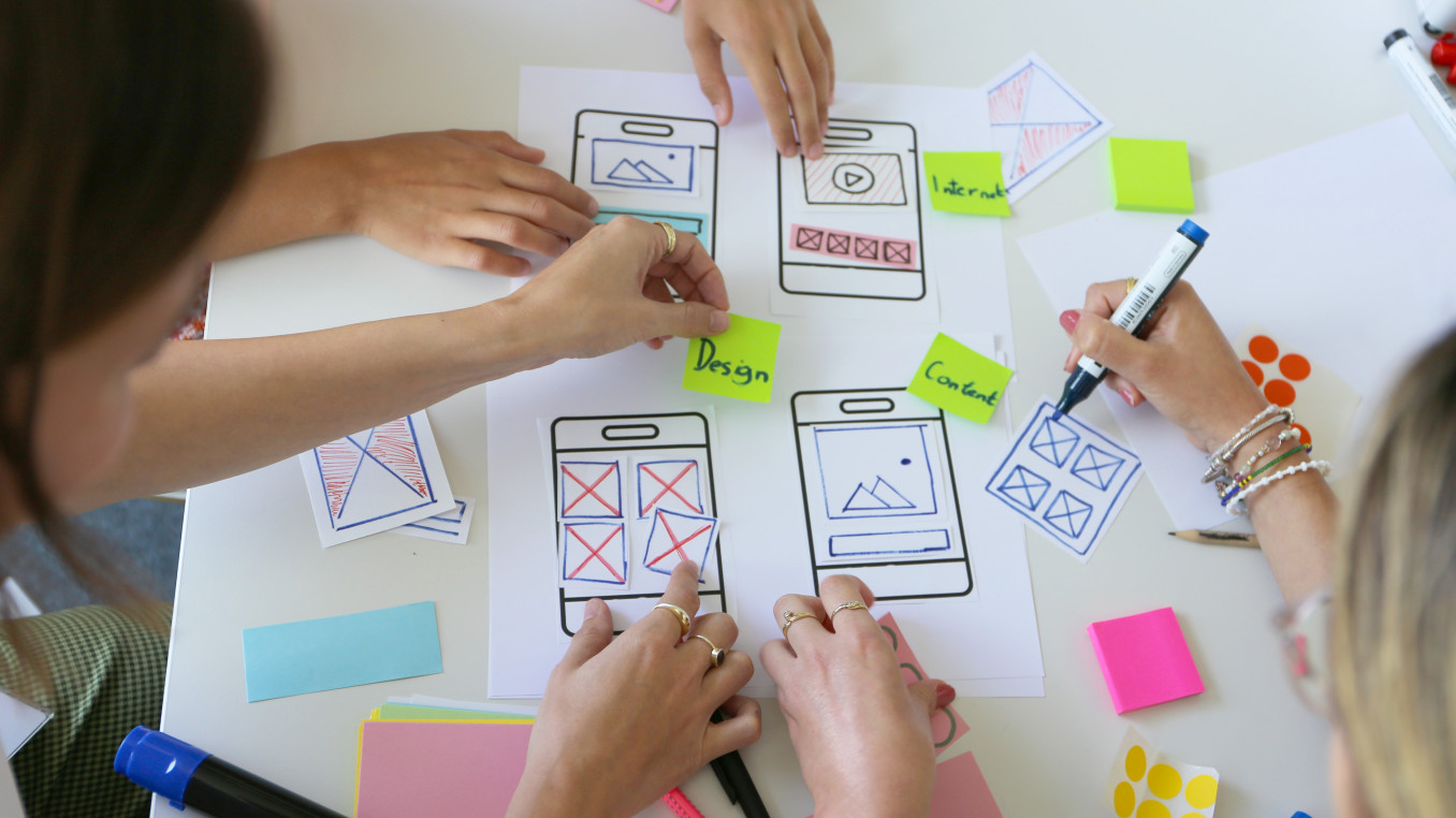 Drei Personen arbeiten an einen Papier-Prototypen für eine mobile Anwendung. 