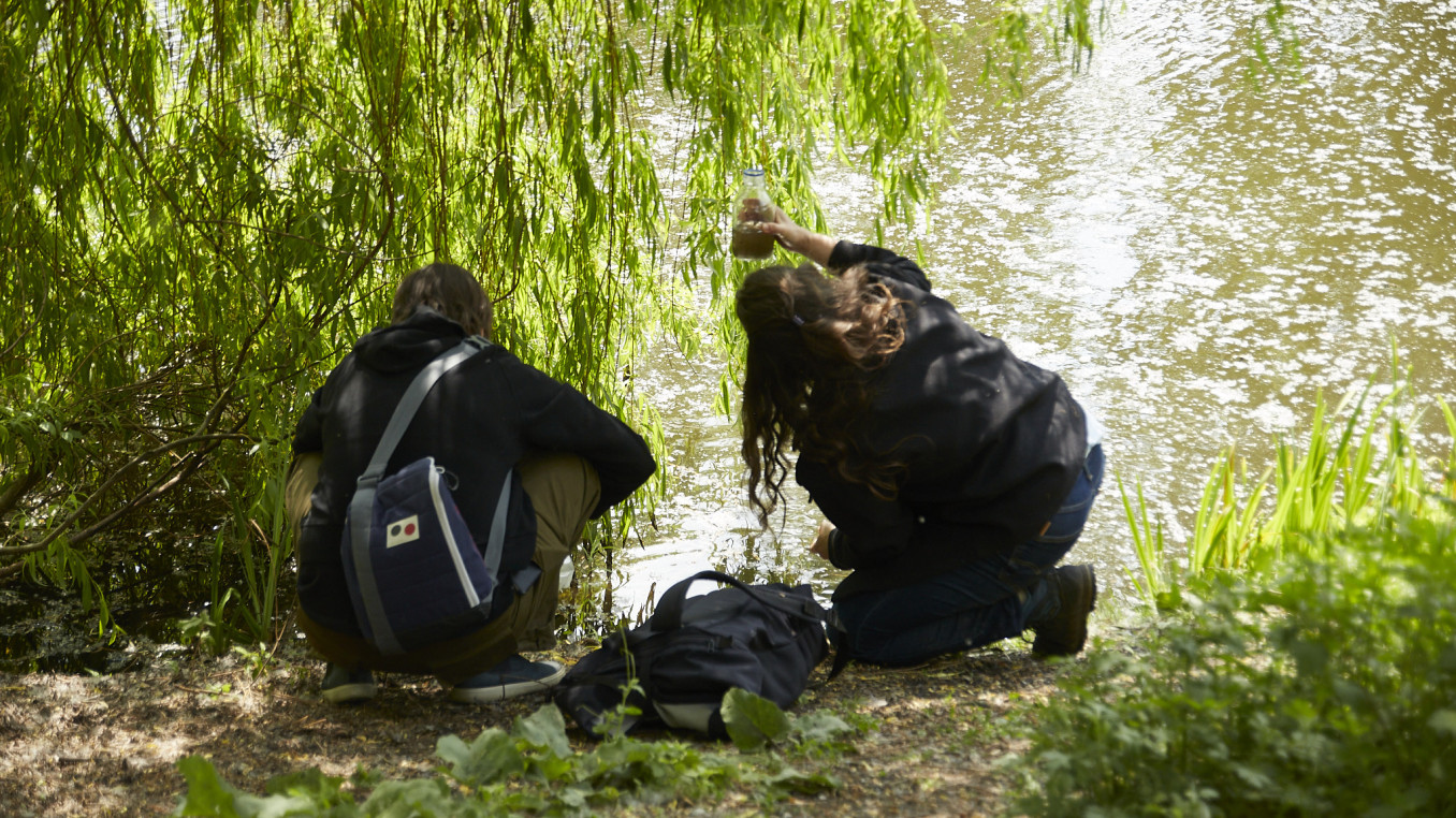 Two people collective water samples from a pond