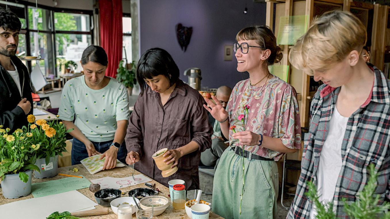 Participants work at a table covered in plants and flowers during a hands-on workshop at SAVVY Contemporary, Berlin.