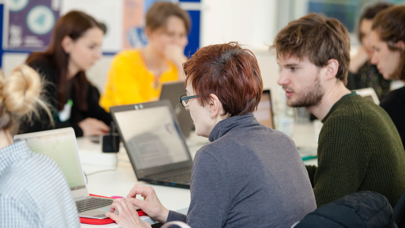 a group of different people in front of computers talking to each other and writing 