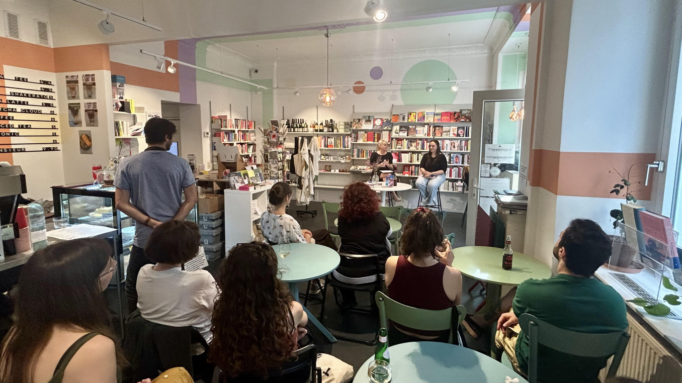 A group of people sitting down around tables, with their backs to the camera, in a book store, listening to a talk
