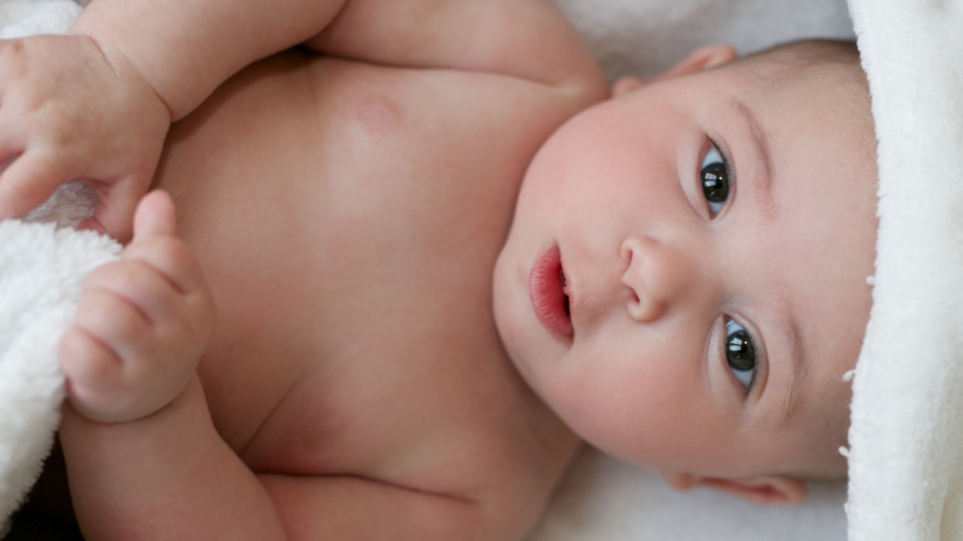 Ein Baby wurde in  ein Handtuch gewickelt und schaut in die Kamera.