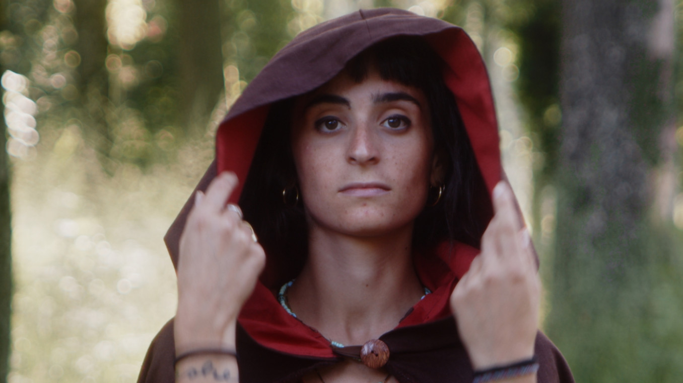 Head and shoulders of a woman in a red hooded cloak with out of focus forest in the background