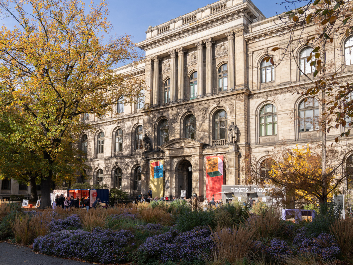 The exterior of a museum with bushes of flowers in front of it.