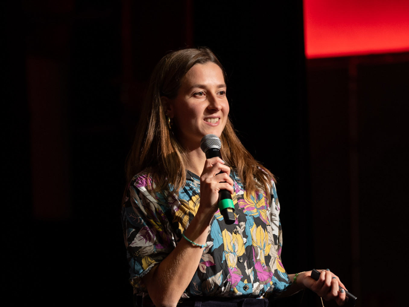 A young woman in a bright shirt holds a microphone as she smiles.