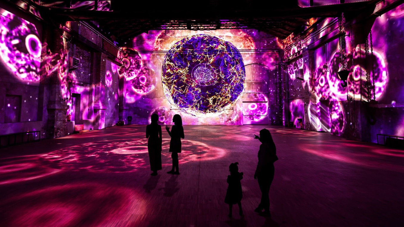 Immersive experience; people standing in a room surrounded by a immersive exhibition